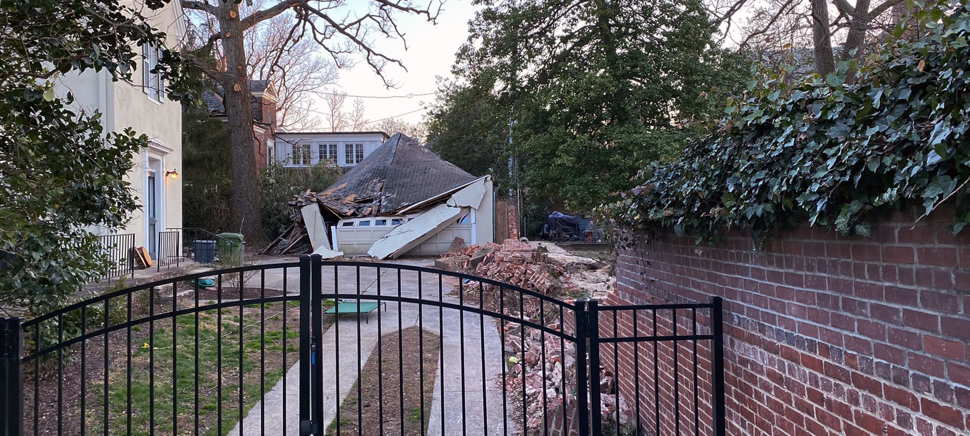 In a wealthy neighborhood, a crushed garage & ruins a of a brick wall