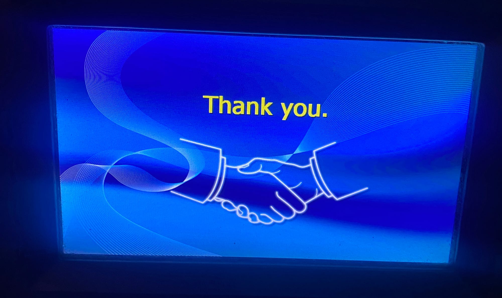 Blue ATM screen. Yellow "Thank You." text sits above a white line drawing of two hands embraced in a business-like shake