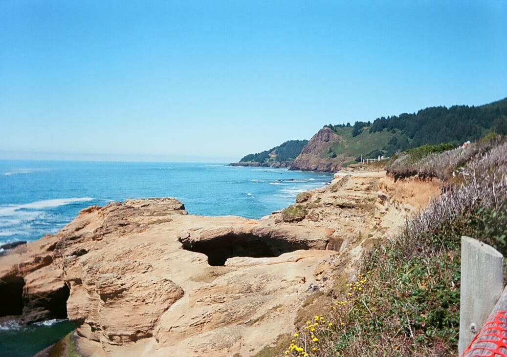 A Big rocky outcropping sticks out into the ocean, there is a large sea cave in the center of the outcropping where you can see down into the water